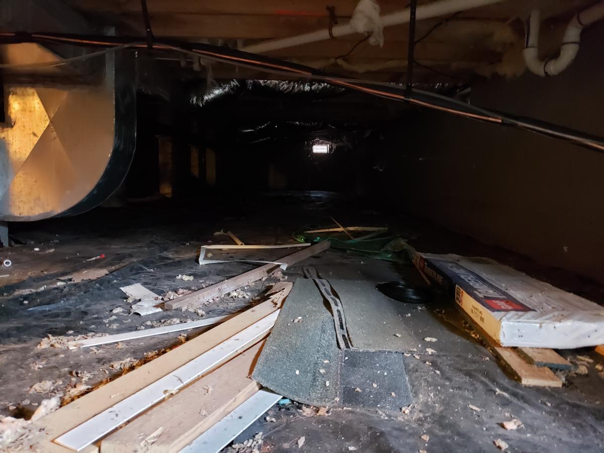 Before full encapsulation project - crawlspace with leftover wood and roof shingles, wiring, white water pipes and air vent